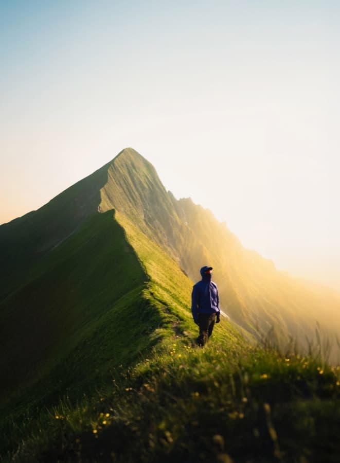 Hiker in tall grass on the backlit Tannhorn ridge