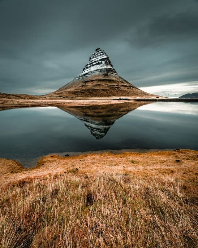 Kirkjufell's cone mirrored in still water above golden grass