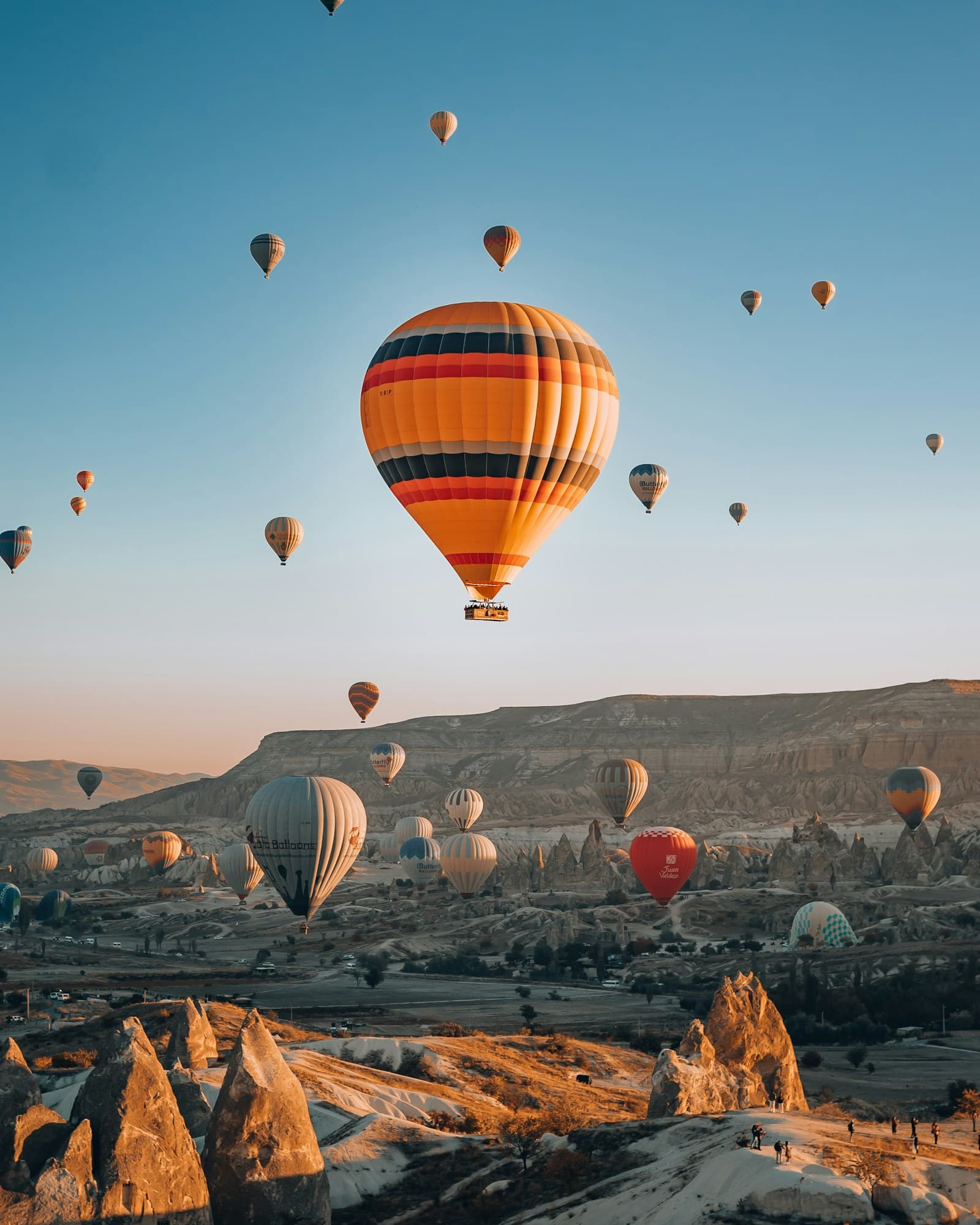 Hot air balloons rising over fairy chimneys and a long flat-topped ridge in Cappadocia at sunrise