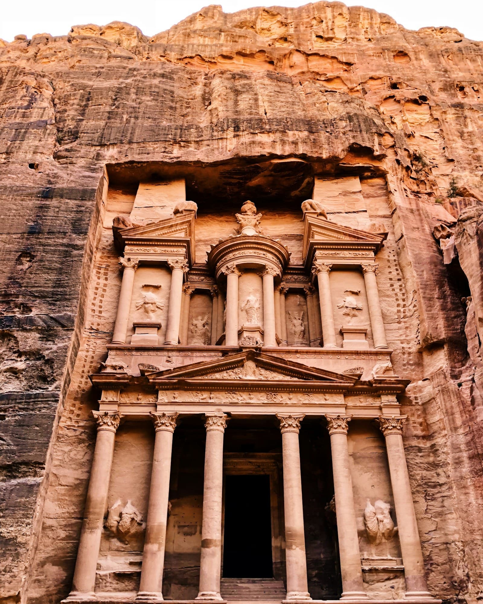 Al-Khazneh, the Treasury of Petra, carved into a rose-red sandstone cliff in warm light