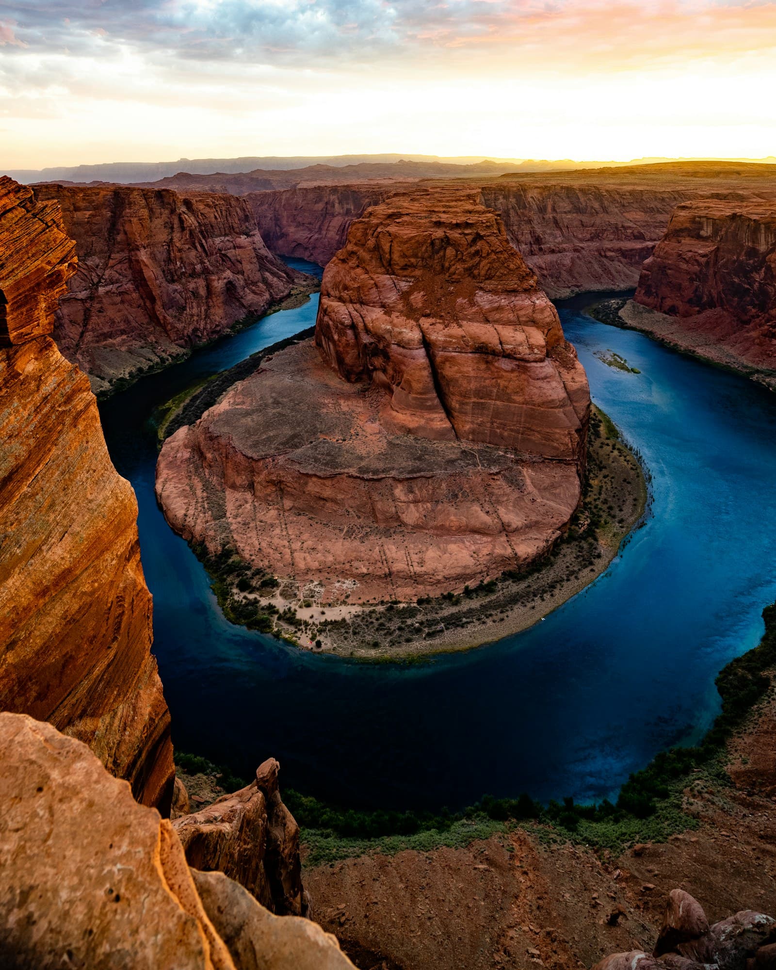 Horseshoe Bend with the Colorado River curving around its sandstone butte under a golden sunset sky near Page