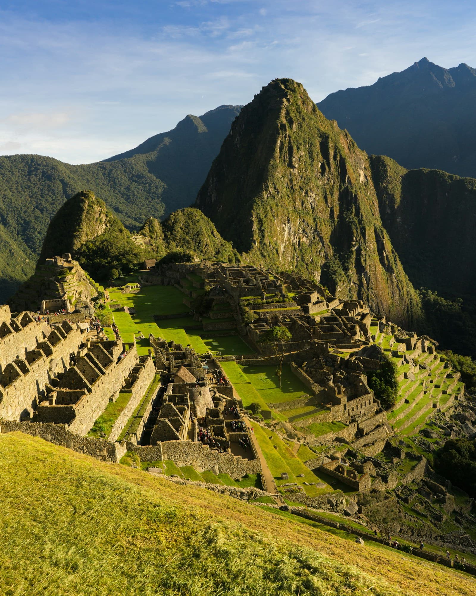 Machu Picchu and Huayna Picchu in low late-afternoon sun, seen from the upper terraces above the city