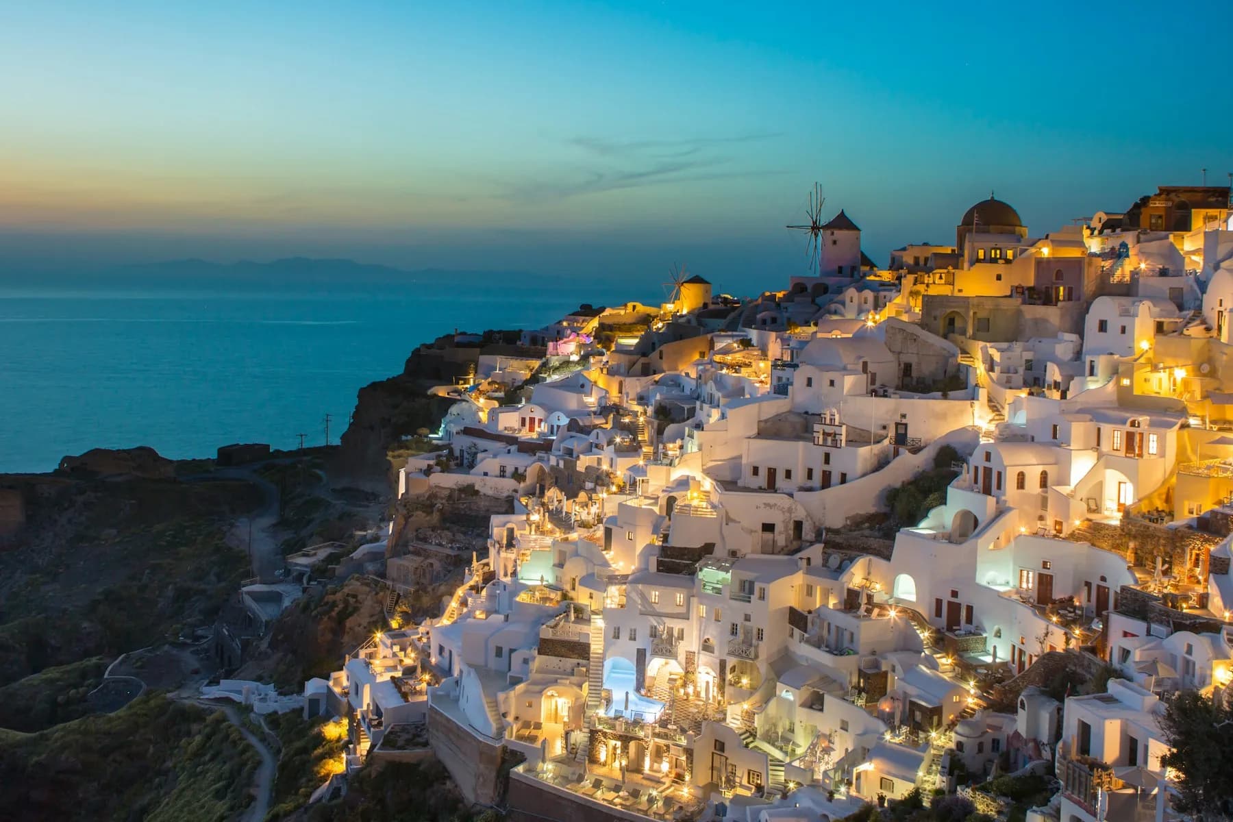 Oia on Santorini at blue hour, lights coming on along the caldera cliff