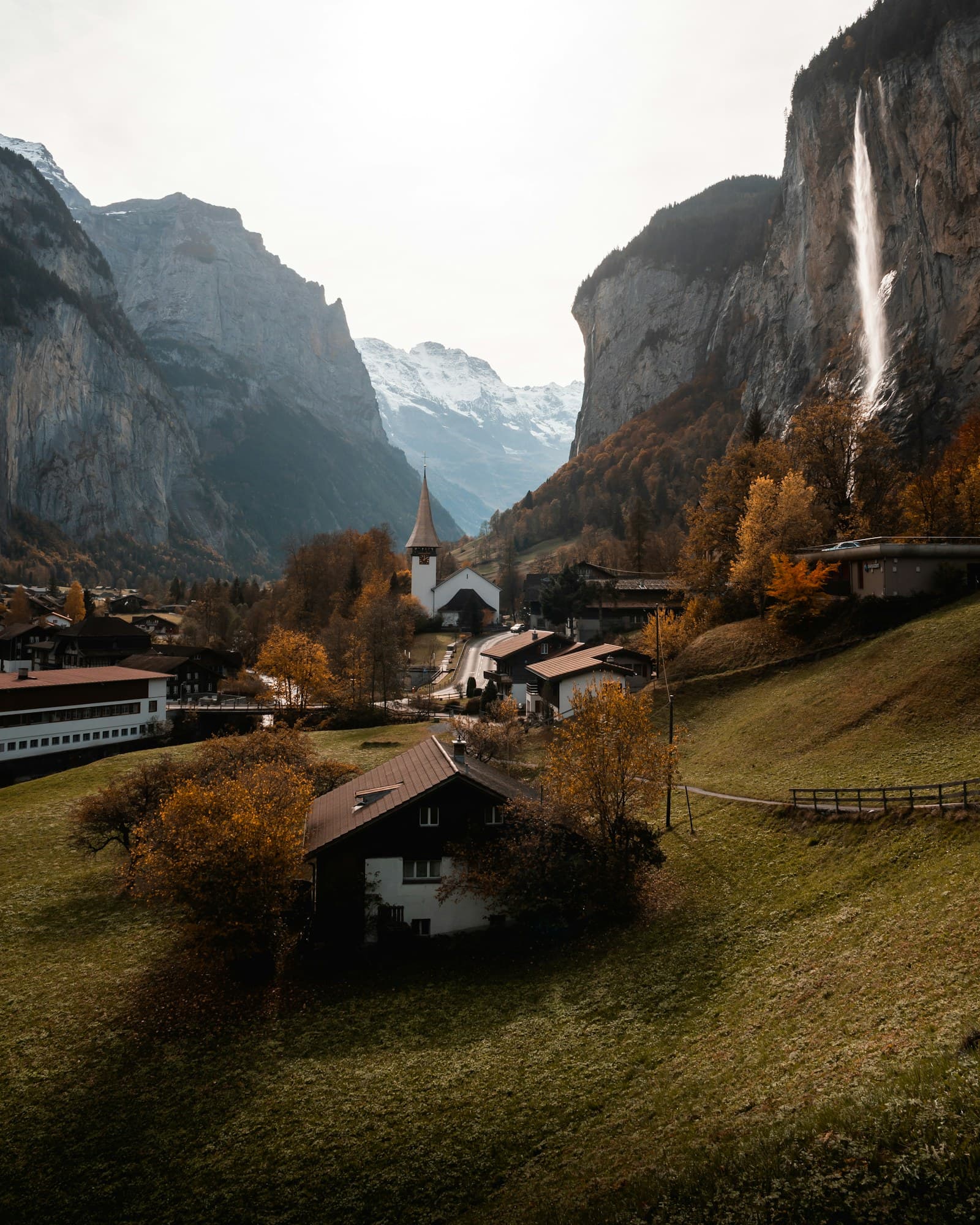 Lauterbrunnen church and Staubbach Falls in autumn light, with snowy peaks closing the valley